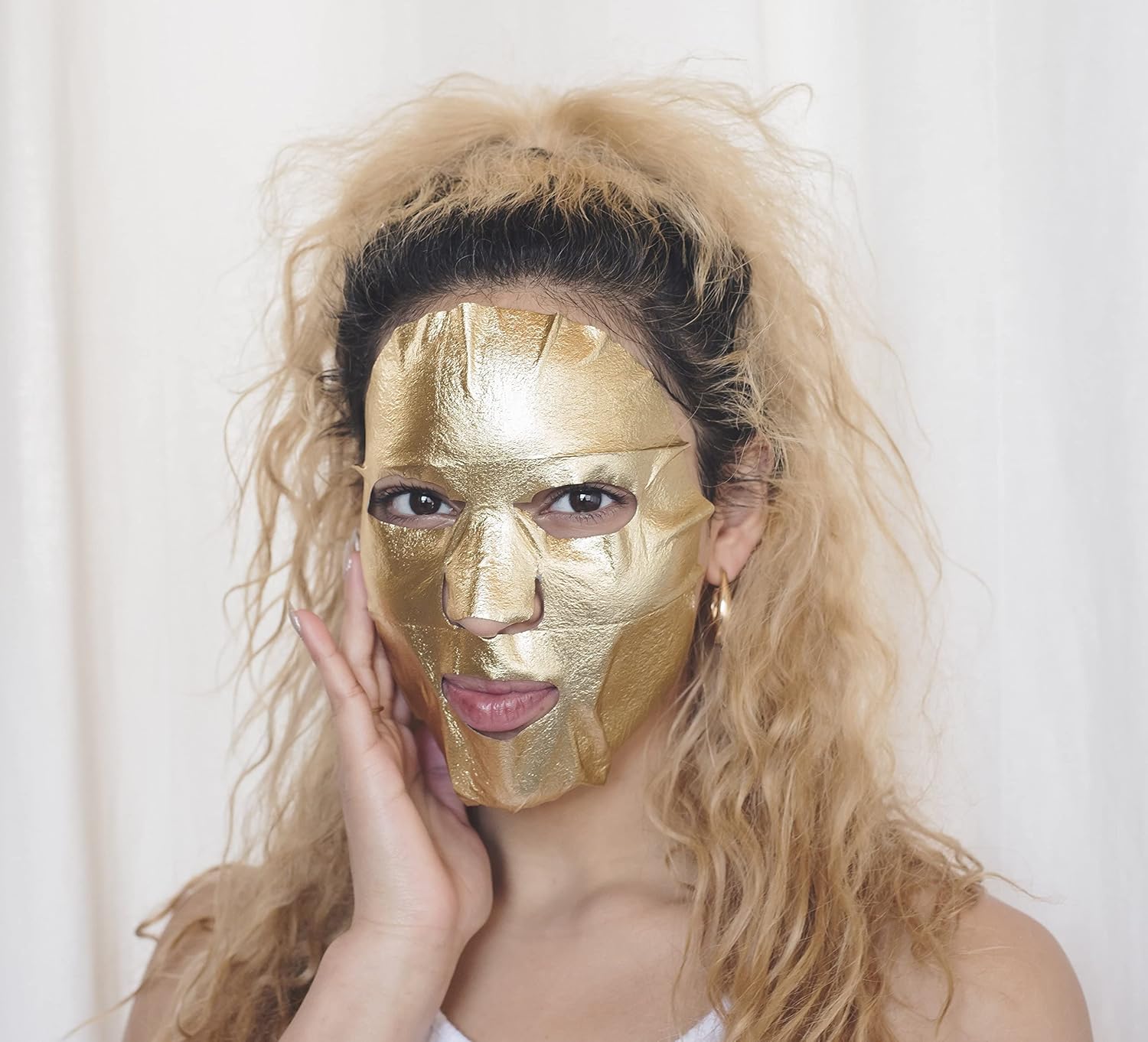 Woman applying Masque Bar Gold Foil Sheet Mask, designed to brighten dull skin and provide a radiant, moisturized complexion.