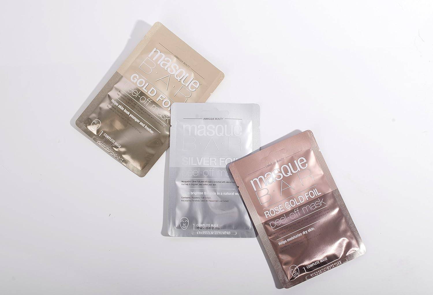 Flat lay of Masque Bar foil peel-off masks in gold, silver, and rose gold variants for detox, glow, and skincare variety.