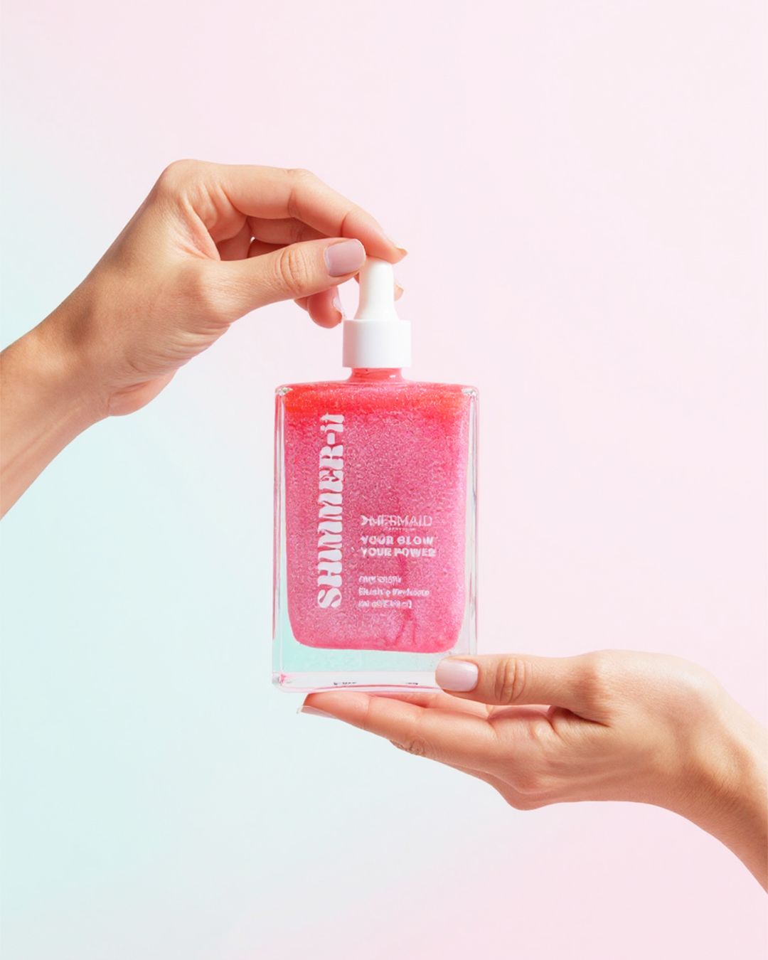 Mermaid Pink Oil - Shimmering Body Oil in a glass dropper bottle held by two hands. Lightweight and perfumed for glowing, smooth skin care.