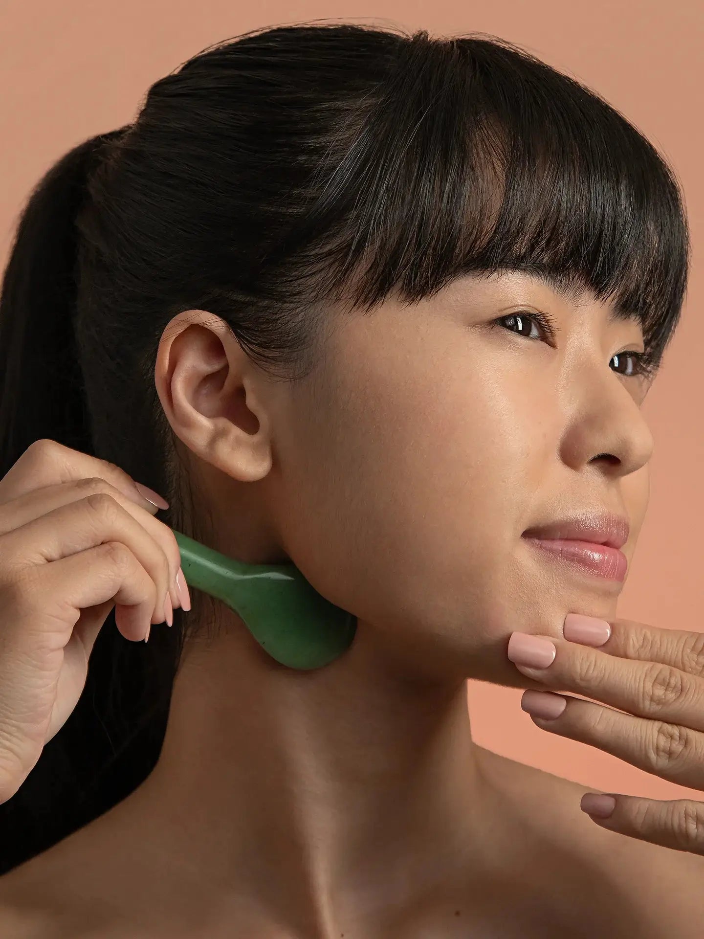 A woman using Mount Lai The Jade Acupressure Gua Sha Spoon on her jawline, demonstrating its benefits for facial massage and circulation.