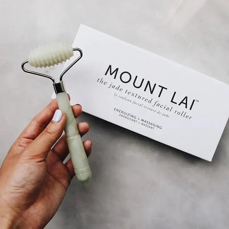 Hand holding Mount Lai The Jade Massage Textured Facial Roller with packaging in the background, emphasizing its ergonomic design and skincare benefits.