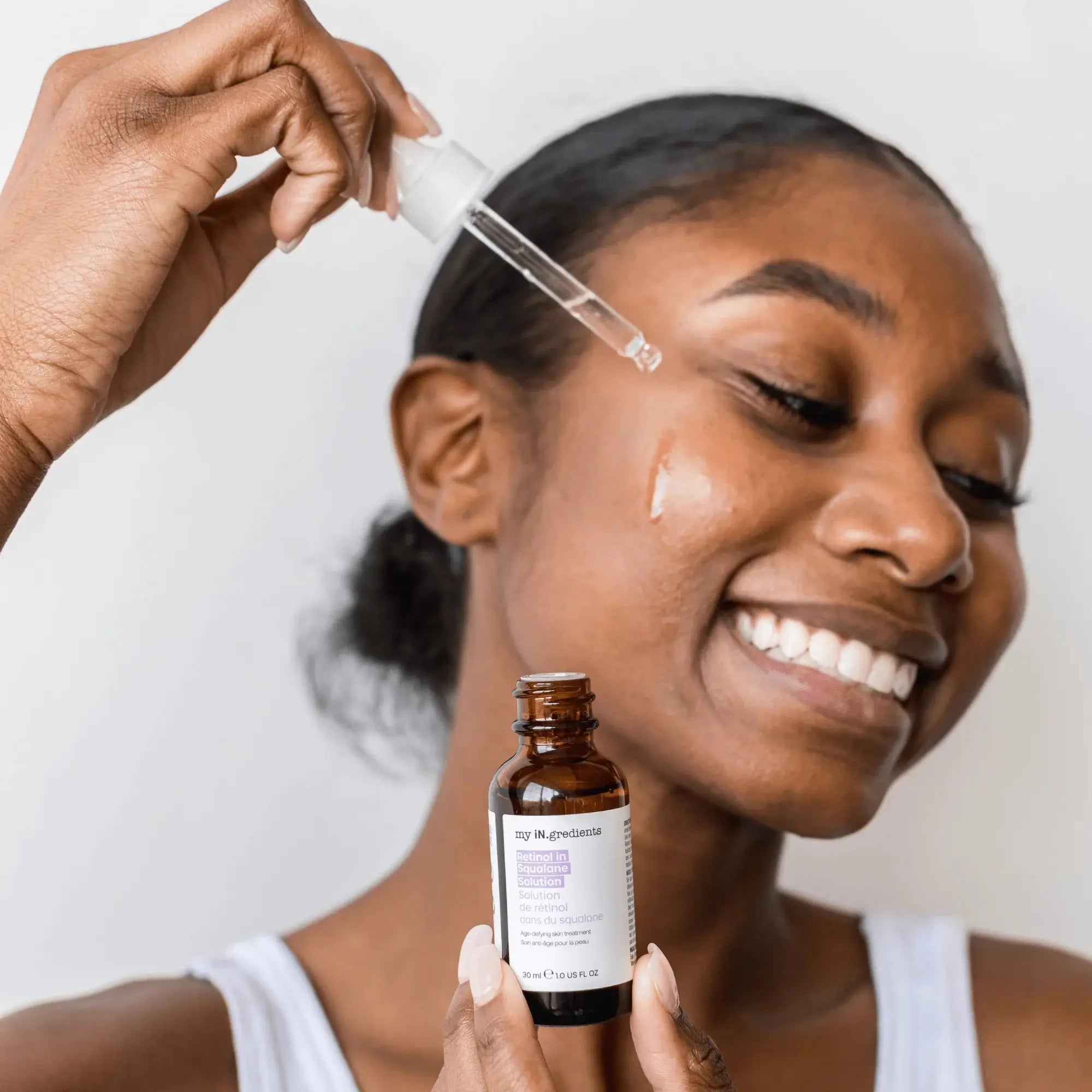 Smiling woman applying My iN.gredients Retinol Squalane Night Treatment serum to face, promoting smooth and refined skin texture.