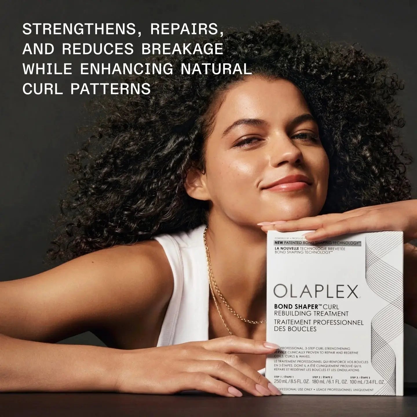Smiling woman with curly hair holding Olaplex Bond Shaper Curl Rebuilding Treatment Kit, emphasizing its strengthening and repair benefits for curls.
