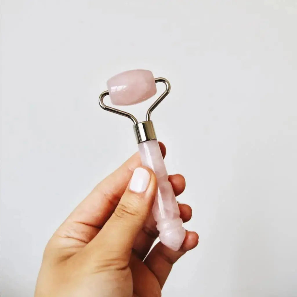 A hand holding the Mount Lai The De-Puffing Mini Rose Quartz Roller, highlighting its compact size and premium rose quartz material for skincare benefits.