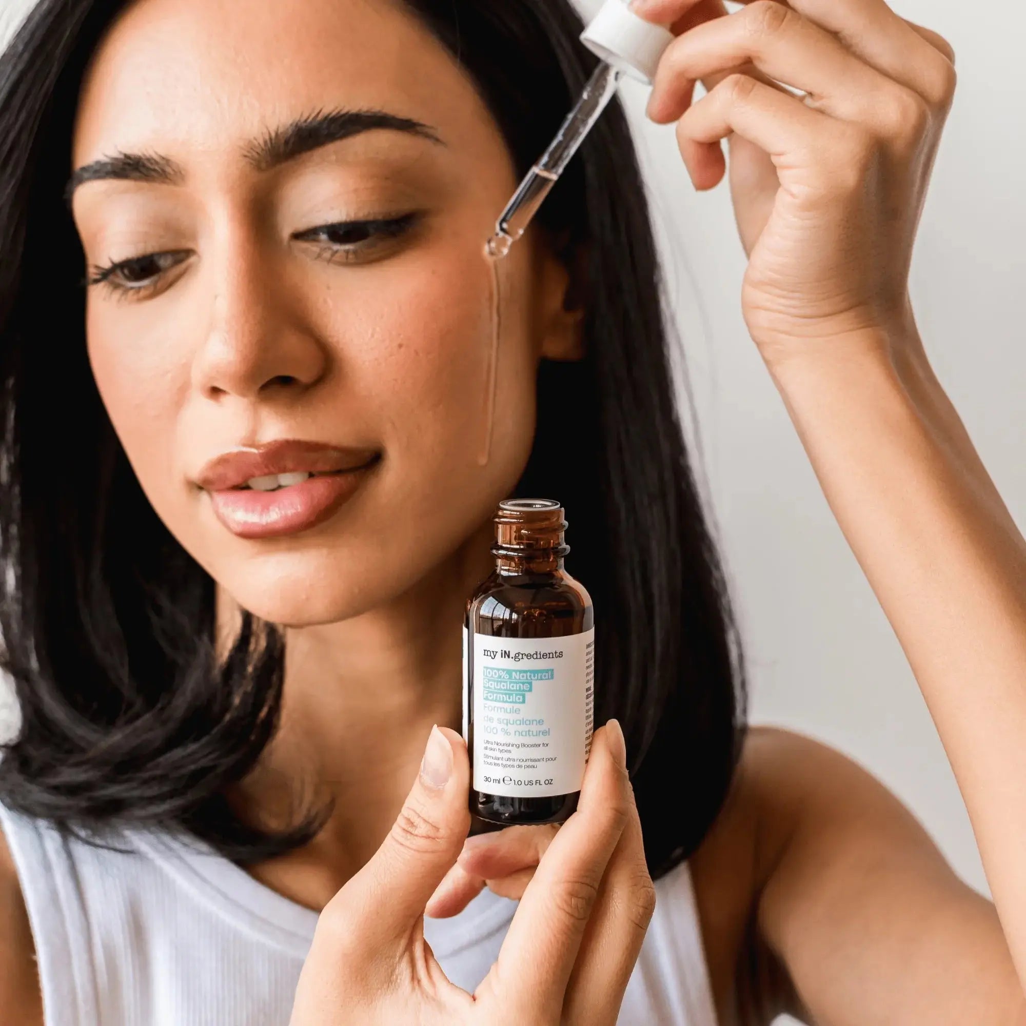 Woman applying My iN.gredients 100% Natural Squalane Serum to face using dropper, showcasing skincare routine for hydration.