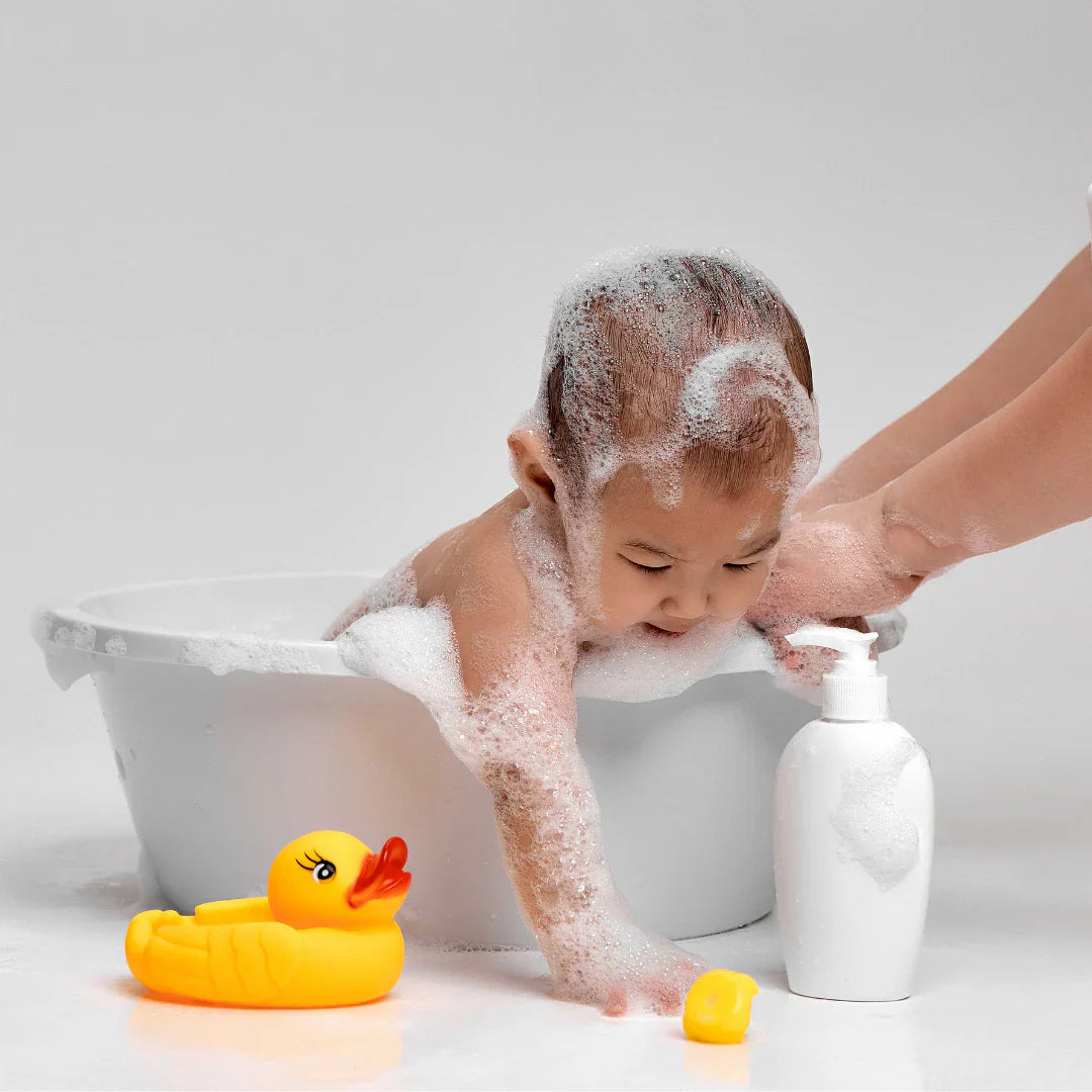 Adorable baby in bubble bath with rubber duck and baby wash bottle.
