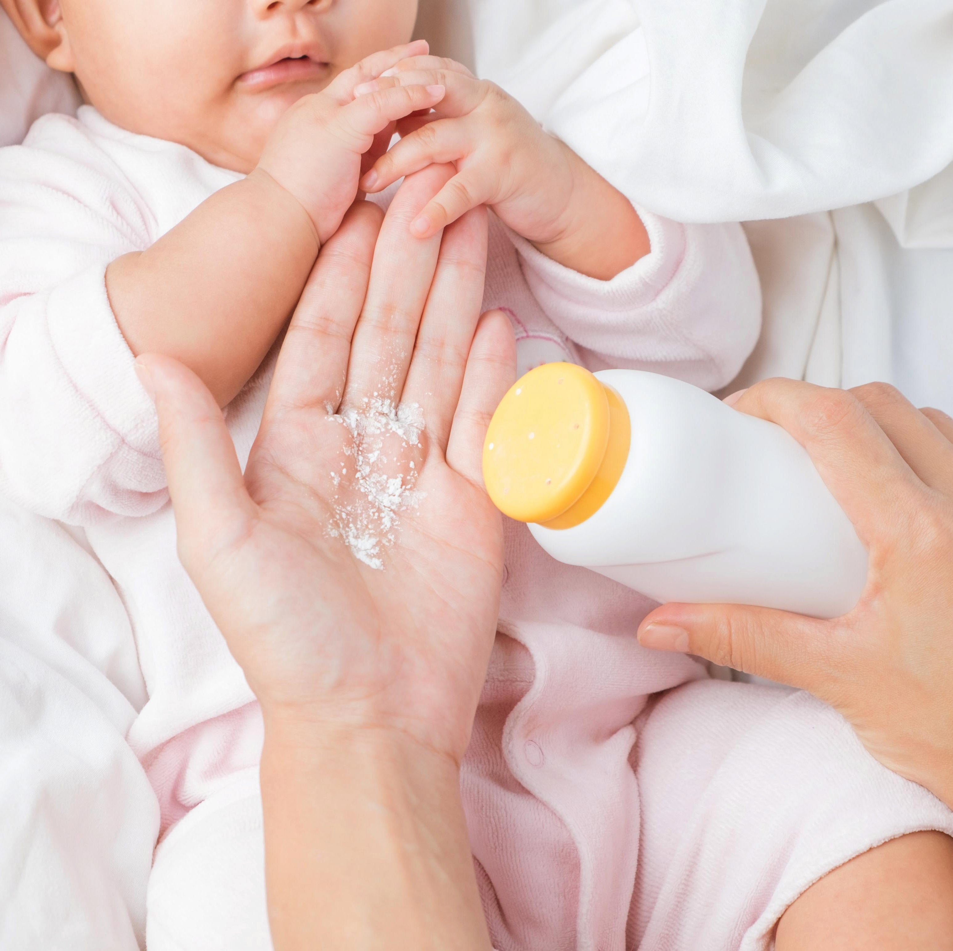 Gentle baby powder applied to infant's hand for soft, fresh skin.