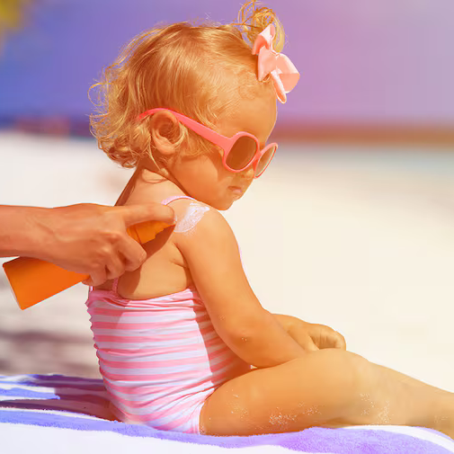 Baby wearing sunglasses gets sunblock applied at the beach.