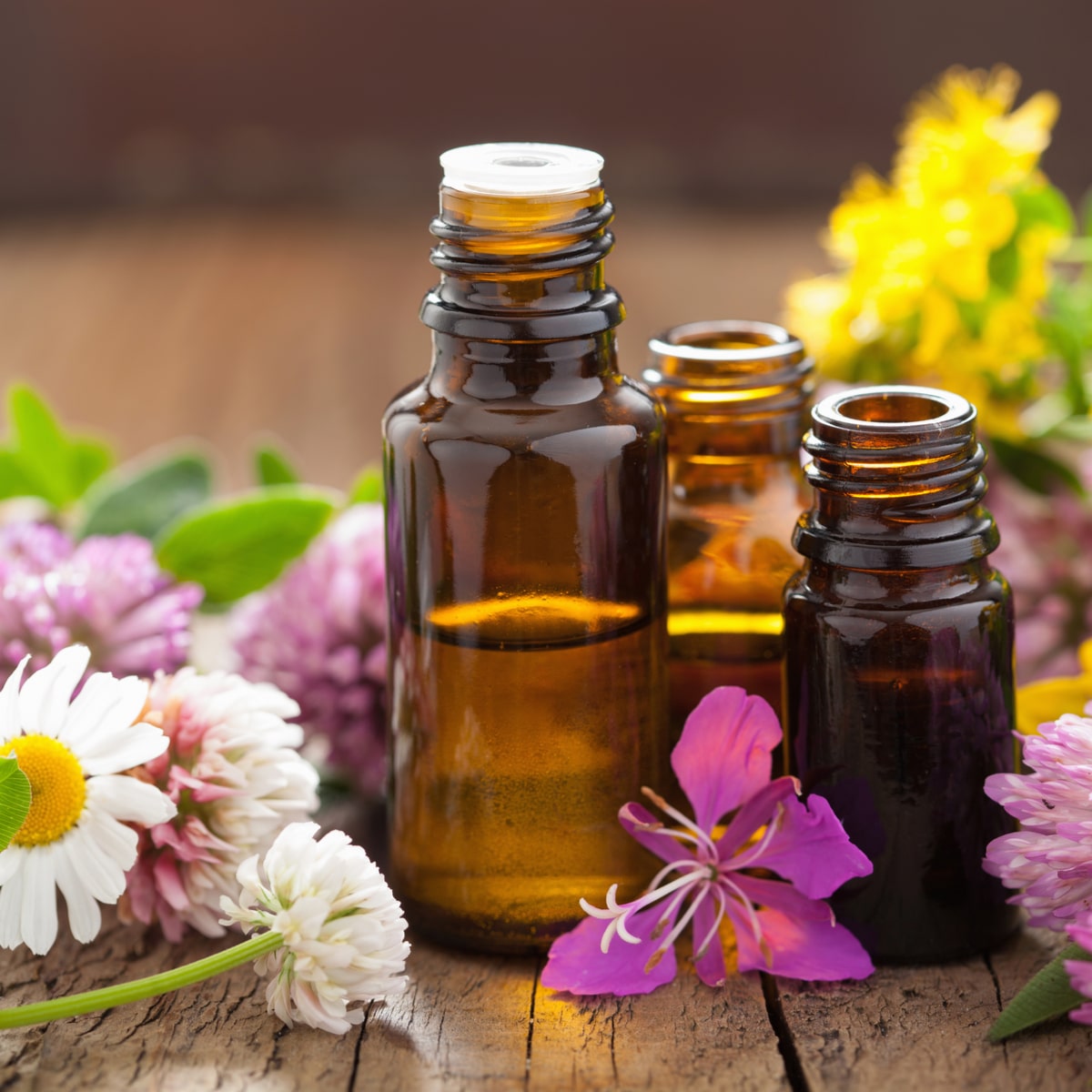 Amber essential oil bottles with fresh colorful flowers on wood.