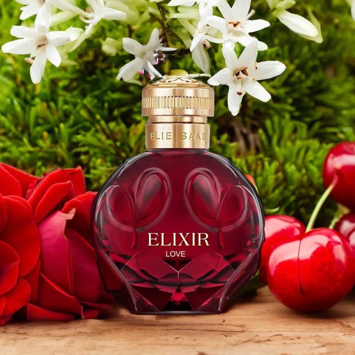 Elie Saab Elixir Love Perfume surrounded by jasmine, roses, and cherries, emphasizing its floral and fruity fragrance composition.