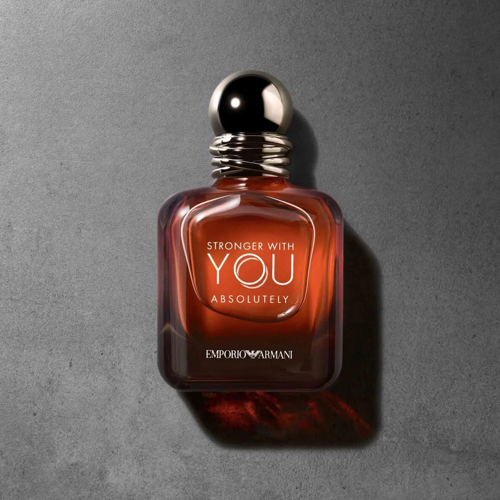 Emporio Armani Stronger With You Absolutely Parfum bottle on a grey surface, showcasing its elegant amber-toned design.