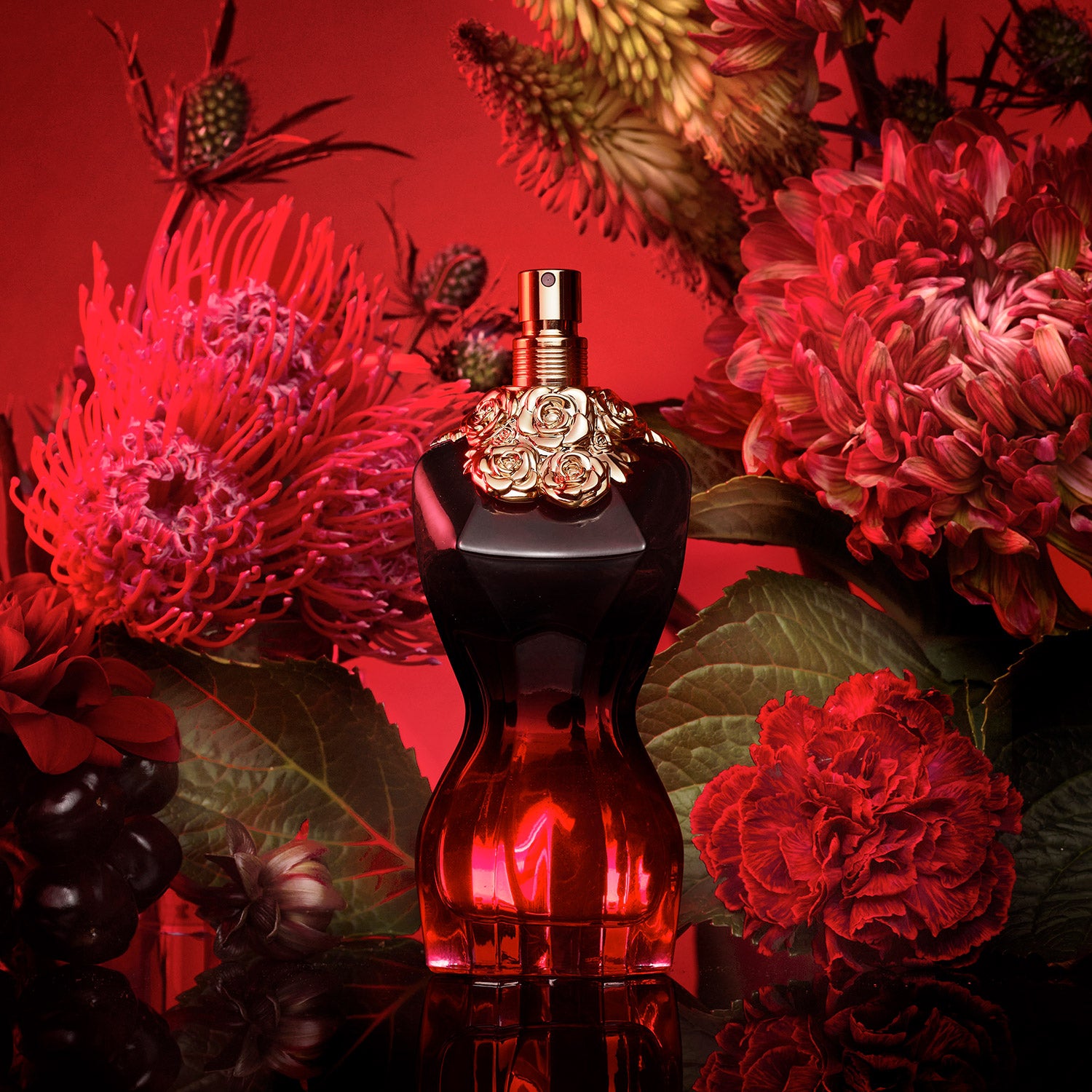 Jean Paul Gaultier La Belle Le Parfum Intense EDP bottle surrounded by red flowers, emphasizing its sensual floral and vanilla fragrance.