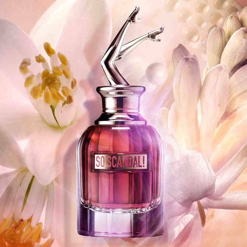 So Scandal Perfume - Jean Paul Gaultier bottle surrounded by jasmine, tuberose, and orange blossom, emphasizing its floral fragrance notes.