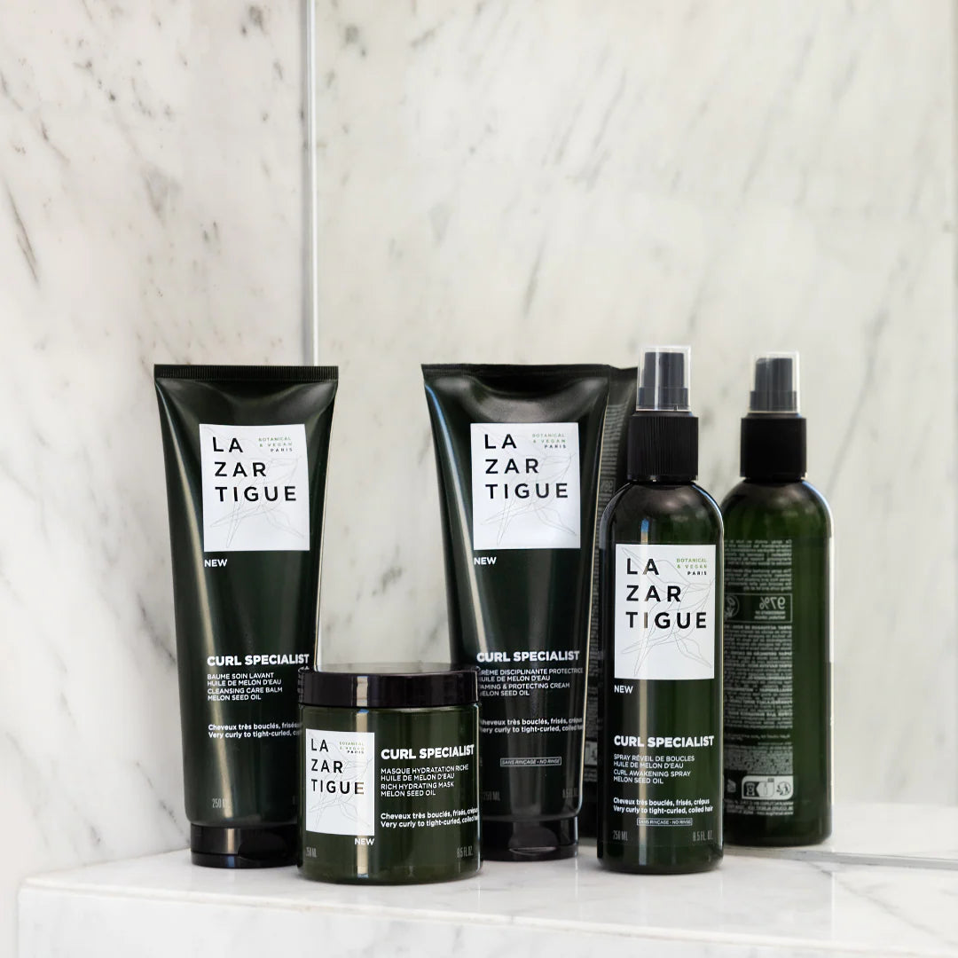 Lazartigue Curl Specialist product line on marble counter, including curl mask, shampoo, and sprays. Complete vegan hair care for curly hair routines.