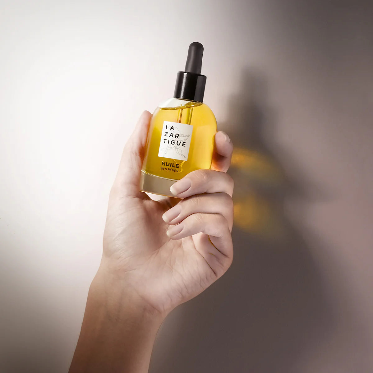 Hand holding Lazartigue Hair Oil - Nourishing Vegan Shine 50 ml, a sulfate-free, paraben-free treatment for soft, glossy hair.