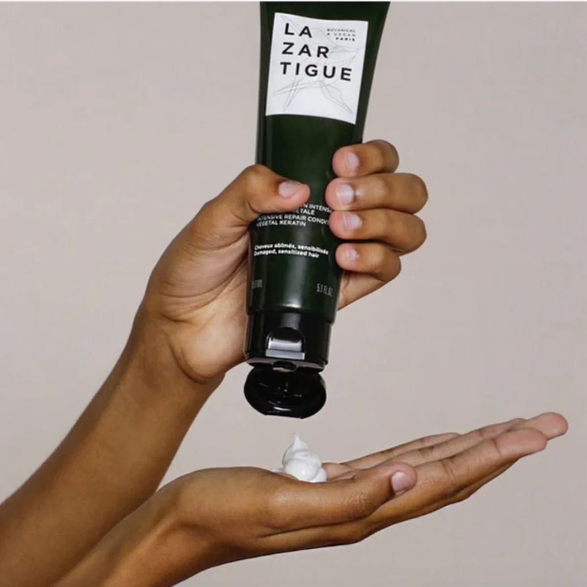 Person dispensing Lazartigue Repair Conditioner into hand, showcasing creamy texture for deep repair of damaged and sensitized hair.