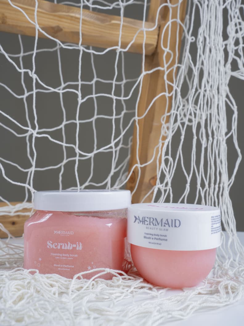 Mermaid Foaming Body Scrub and matching moisturizer displayed on netting, promoting exfoliation and hydration for dry skin.