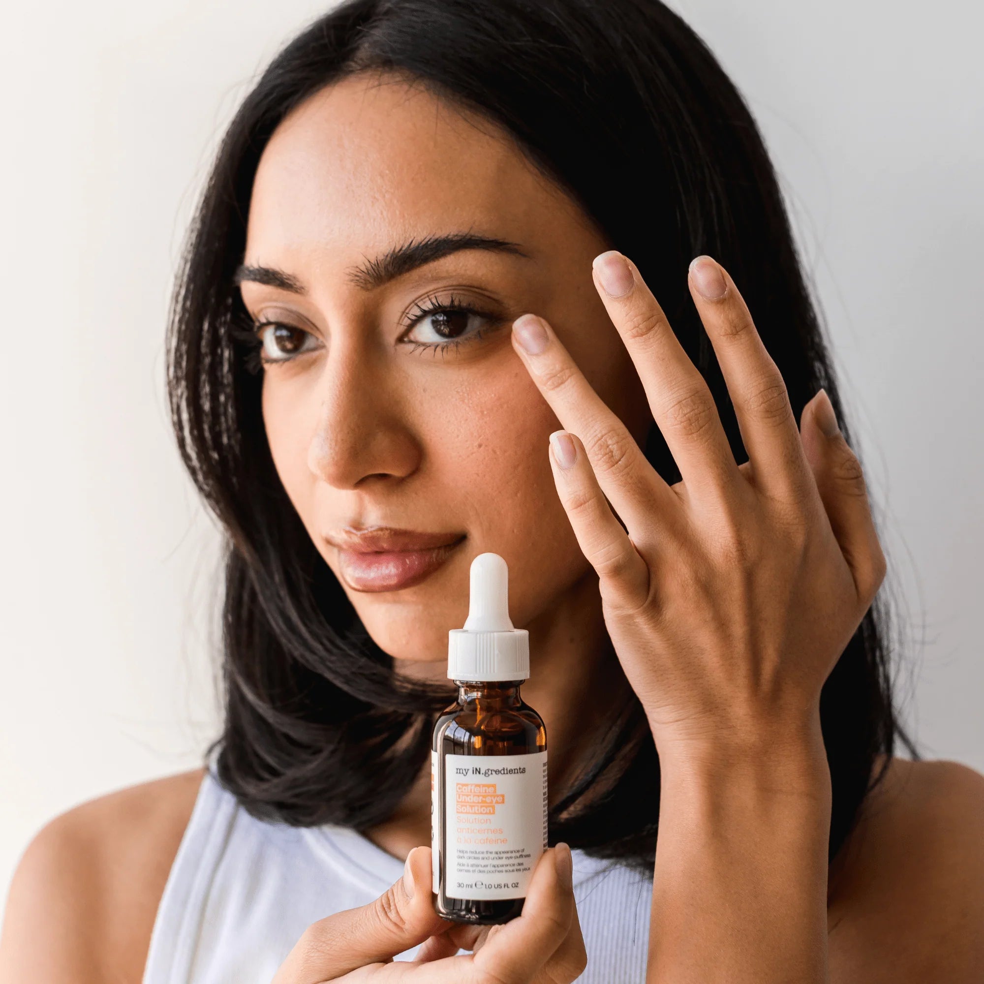 Woman applying iN.gredients Caffeine Under-Eye Solution to under-eye area, demonstrating skincare routine for puffiness and dark circles.