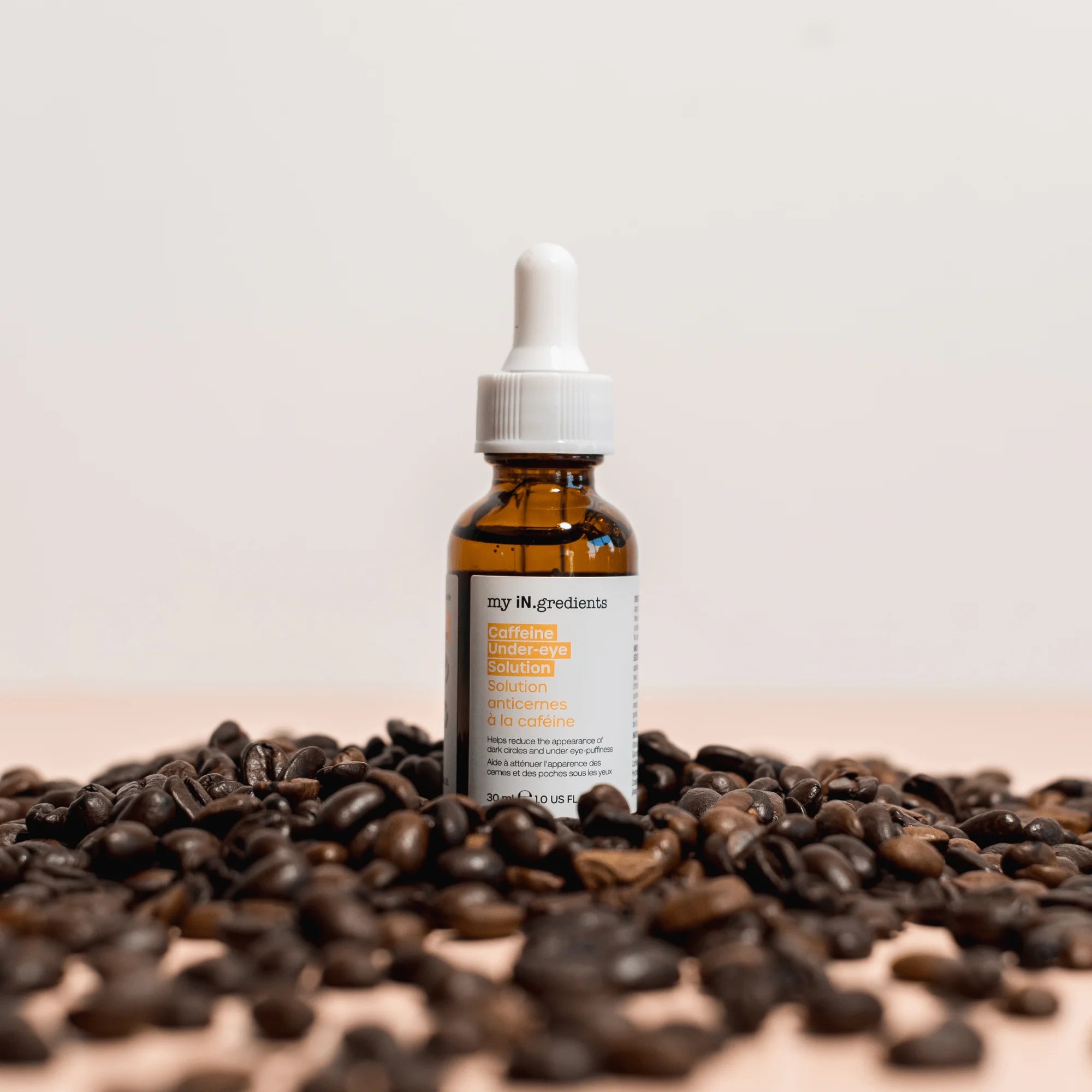 iN.gredients Caffeine Under-Eye Solution bottle surrounded by coffee beans, emphasizing caffeine as key ingredient for eye treatment.