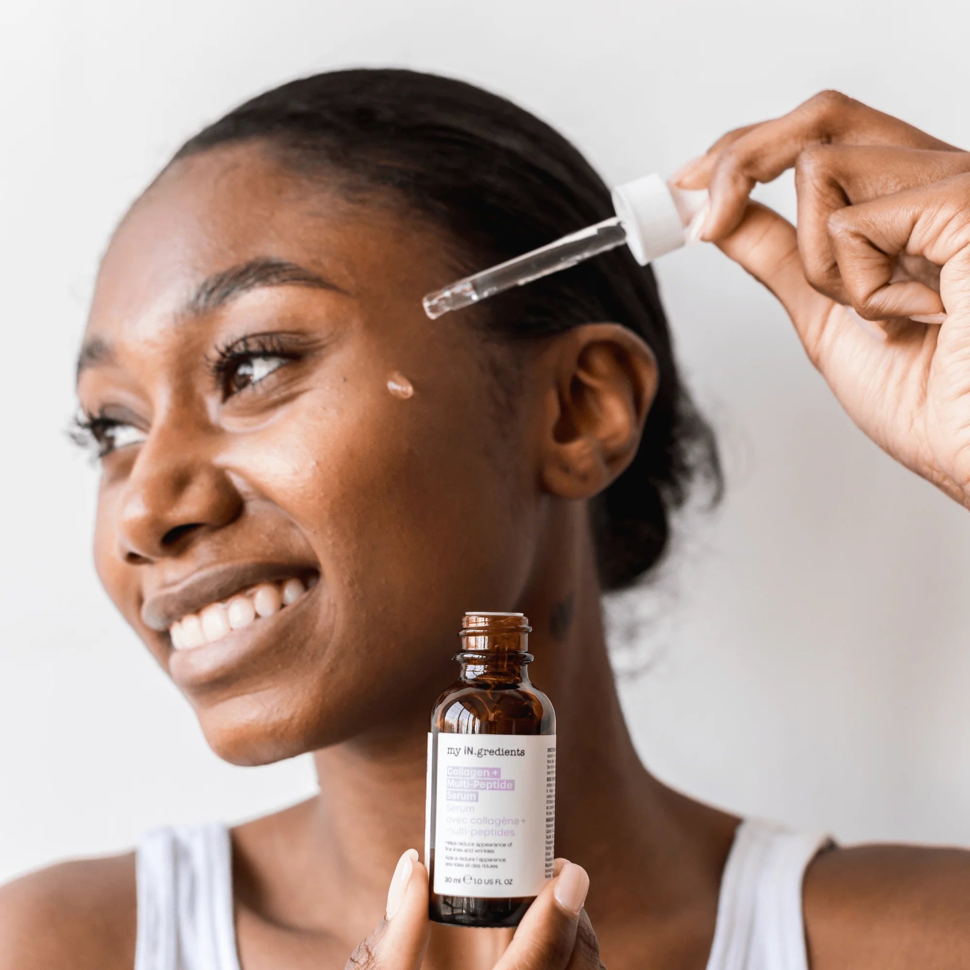 Smiling woman applying My iN.gredients Collagen + Multi-Peptide Serum 30 ml with dropper, promoting skin plumping and pore refinement.