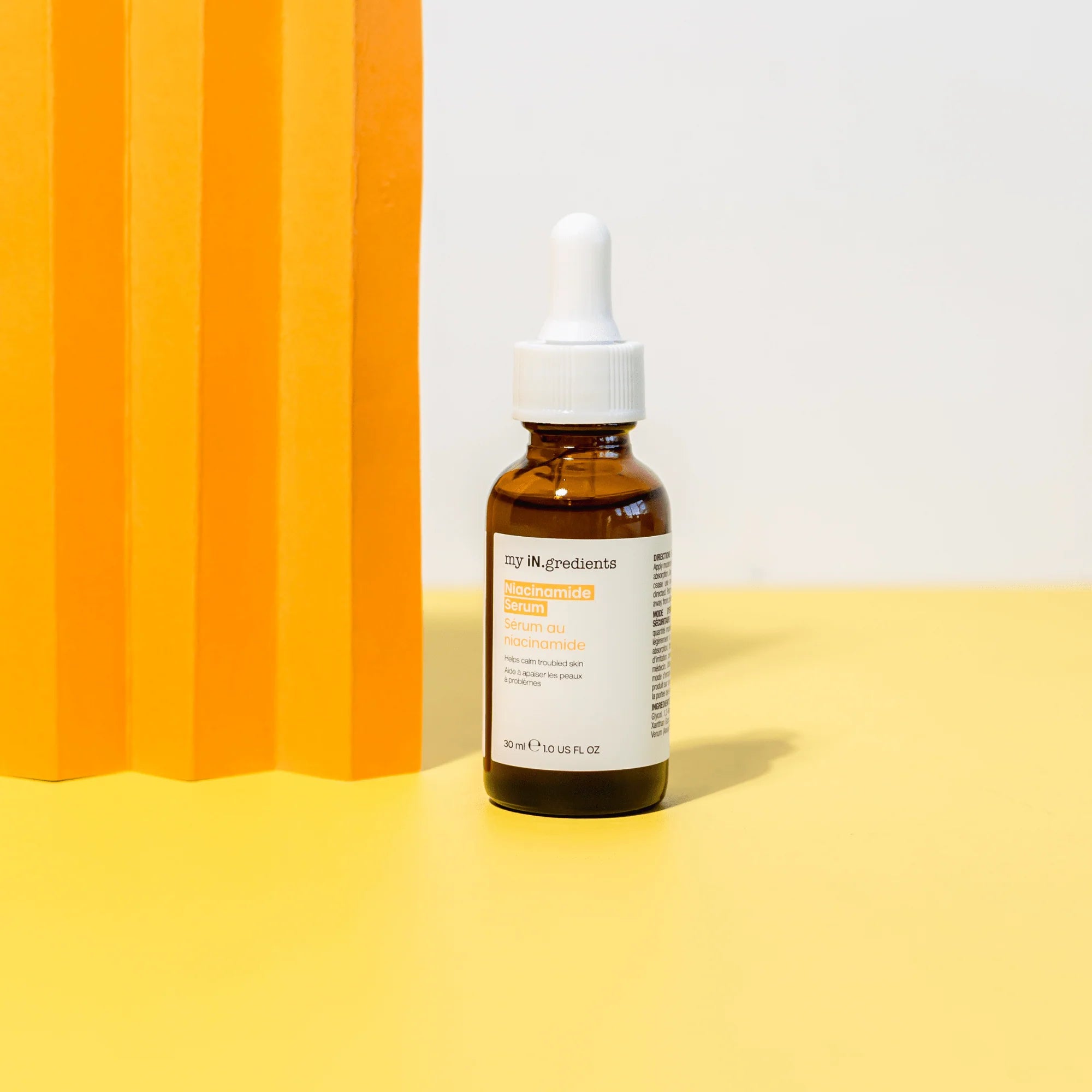 My iN.gredients Niacinamide Serum 30 ml bottle placed on a yellow surface with an orange backdrop, enhancing skincare routines.