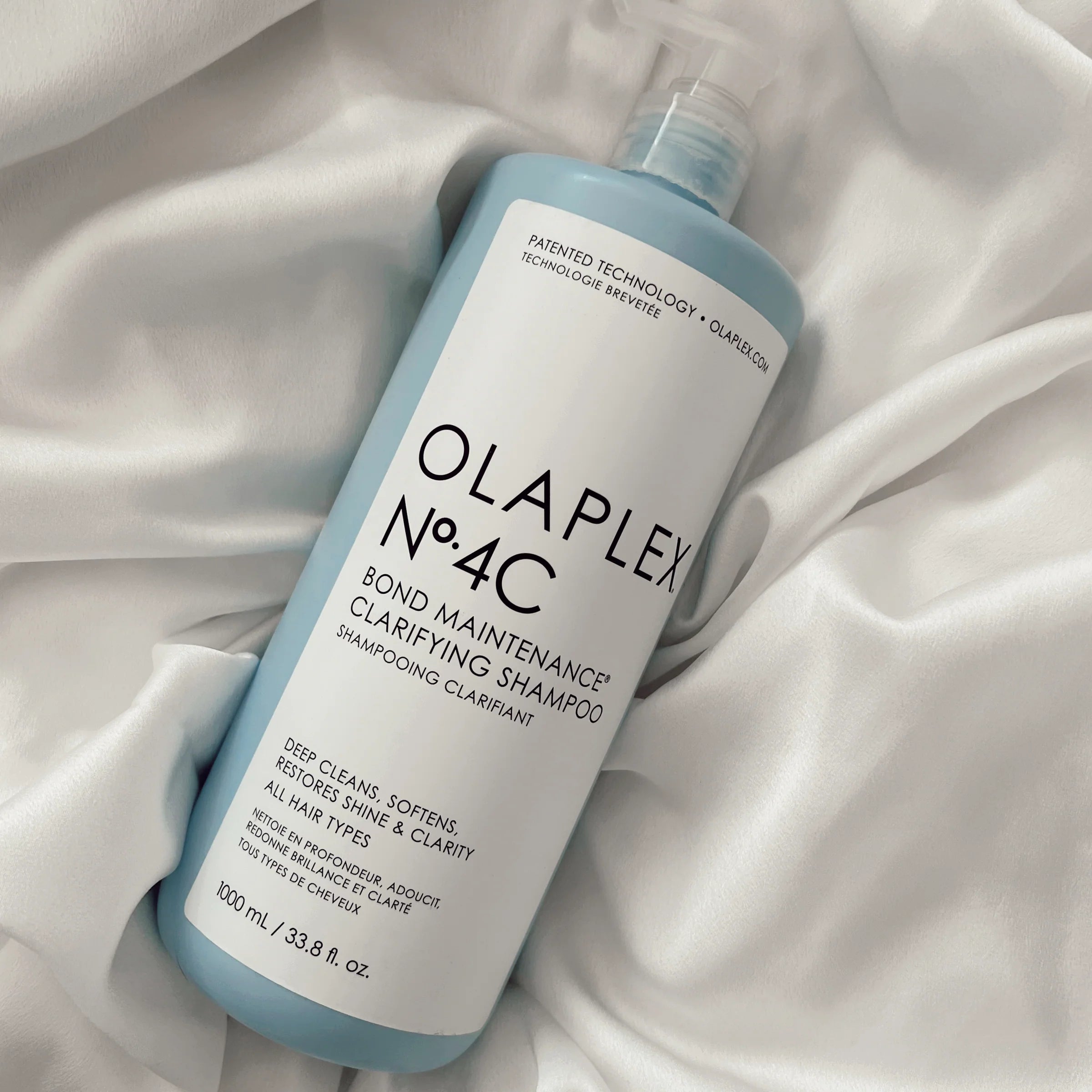 Olaplex No.4C Clarifying Shampoo 1000 ml bottle on white satin fabric, designed to detox and soften damaged or color-treated hair.