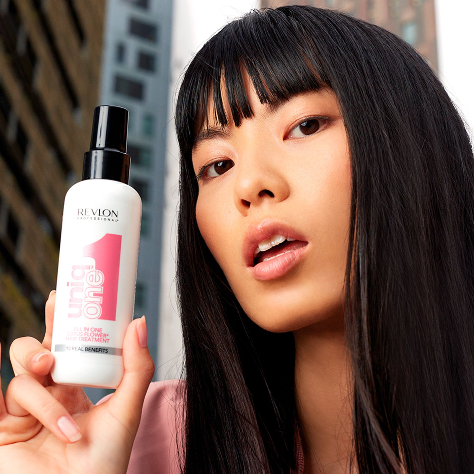 Model holding Revlon Uniq One Lotus Leave-in 150 ml, promoting healthy, smooth hair with all-in-one treatment benefits.