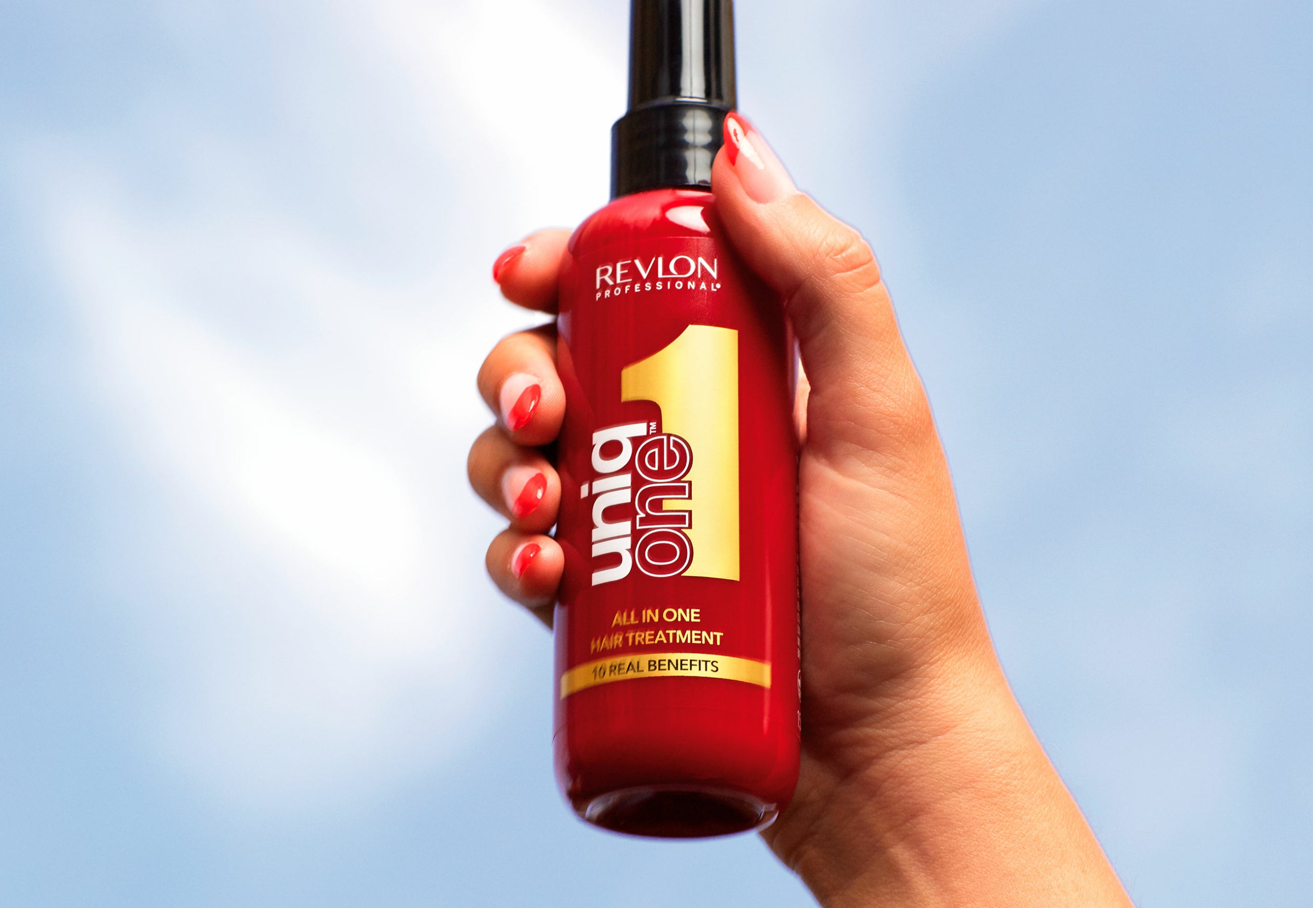 Hand holding Revlon Uniq One Leave-in 150 ml against blue sky, highlighting its all-in-one formula for healthier, manageable hair.