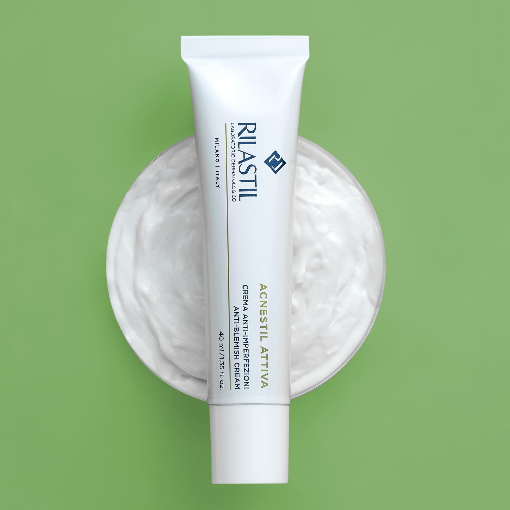 Rilastil Acnestil Anti-Blemish Cream on a green background with open cream jar. Targets acne, enlarged pores, and blemishes with gentle exfoliation.