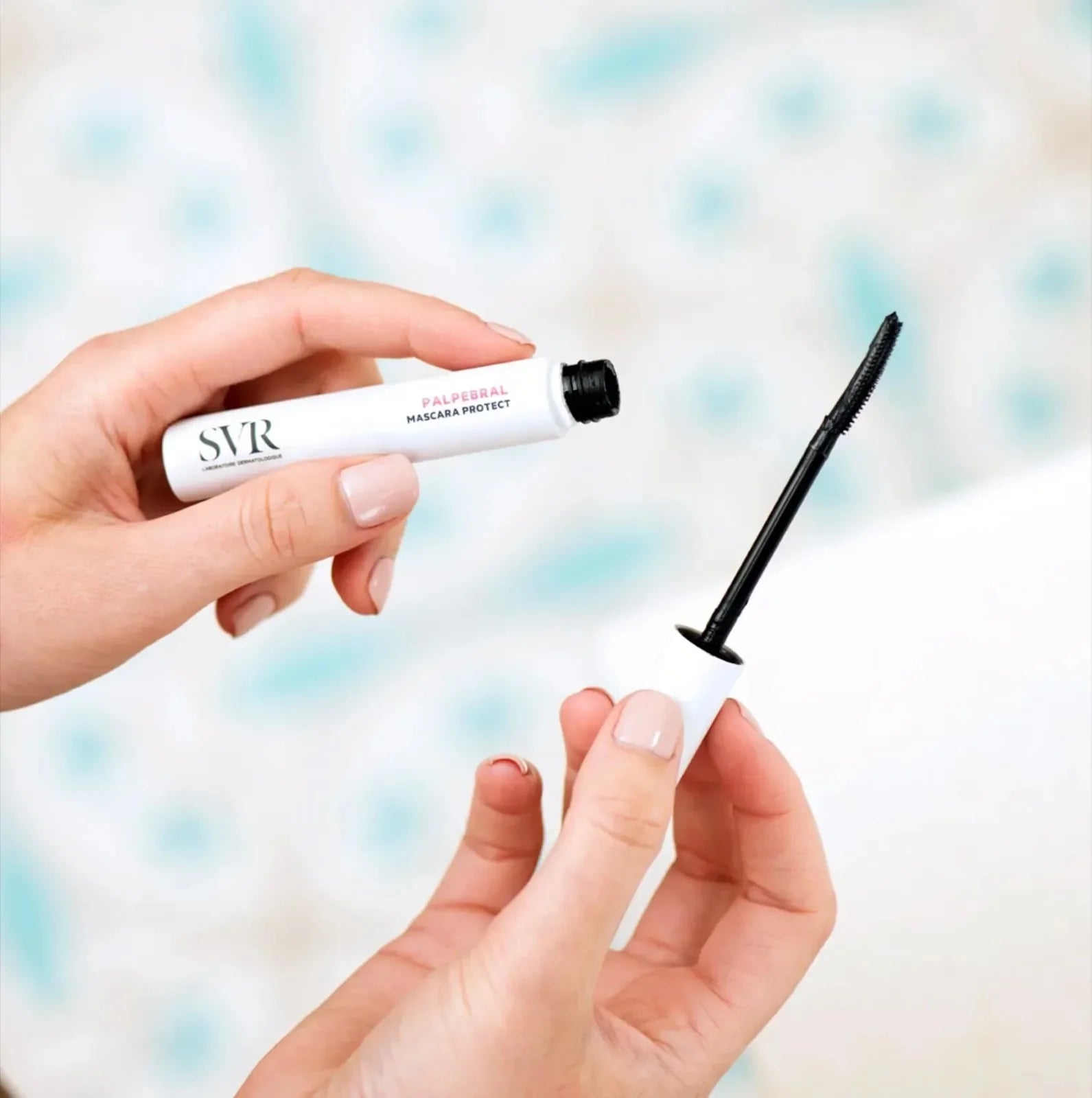 Hands holding SVR Palpebral Mascara with curved applicator, perfect for defining lashes while being gentle on sensitive eyes and skin.