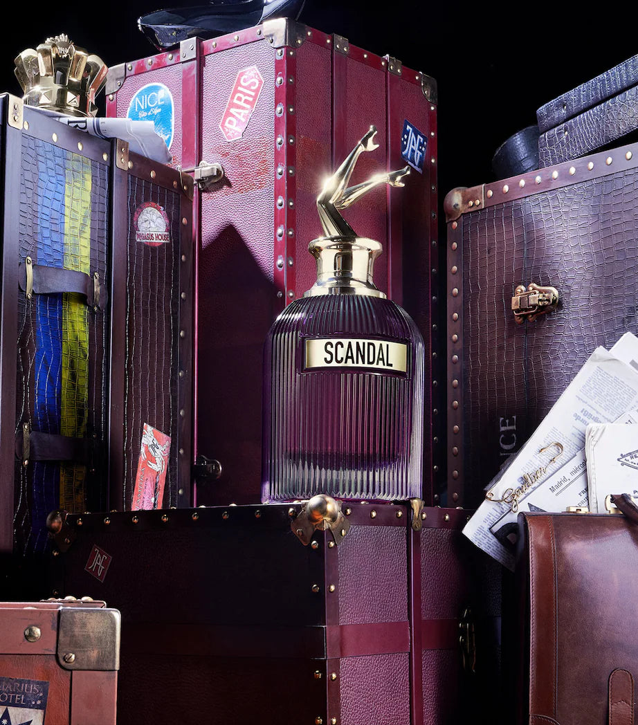 Scandal Intense Floral Perfume by Jean Paul Gaultier displayed among luxury travel trunks, highlighting its bold bottle design and oriental scent.