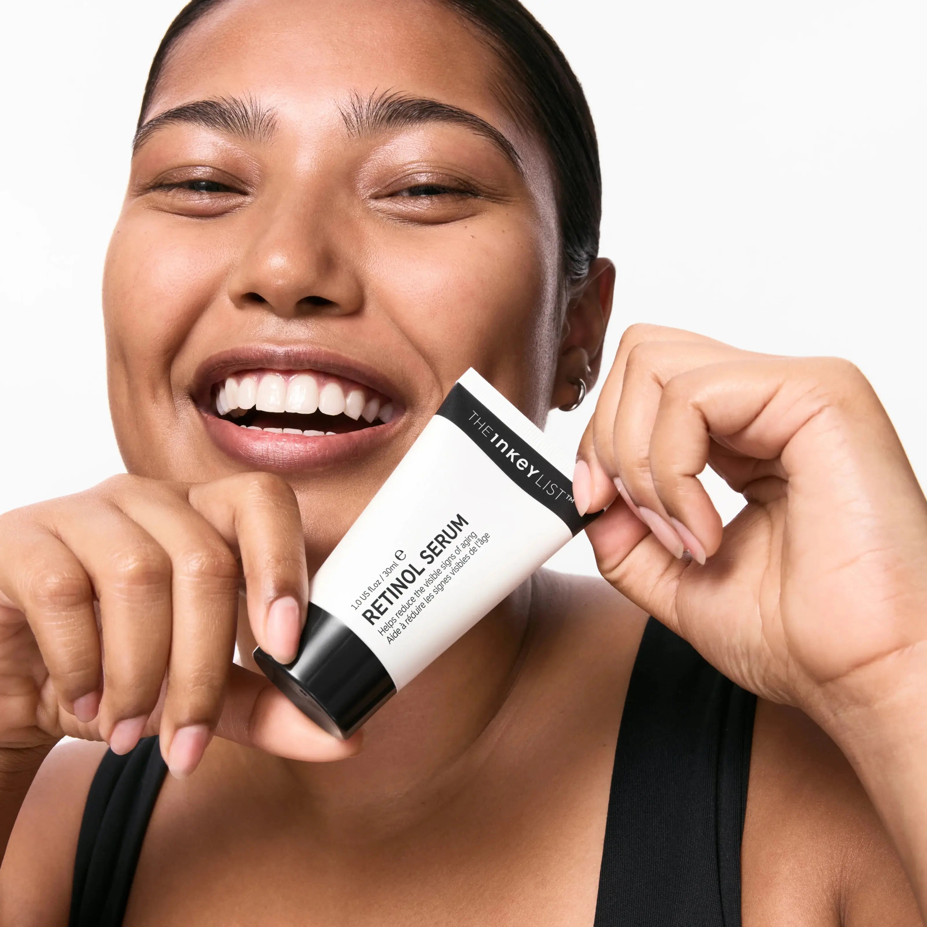 A happy woman holding The Inkey List Retinol Serum 30 ml, highlighting its benefits for reducing wrinkles and evening skin tone. Perfect for all skin types.