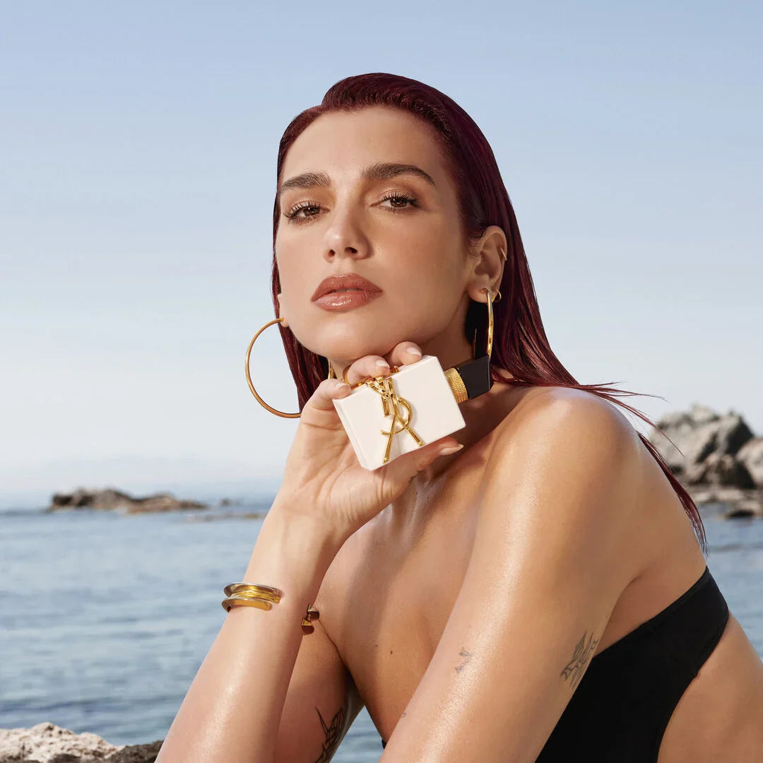 Model holding YSL Libre L'Eau Nue Perfume by the sea, promoting its alcohol-free formula and radiant citrus fragrance for women.