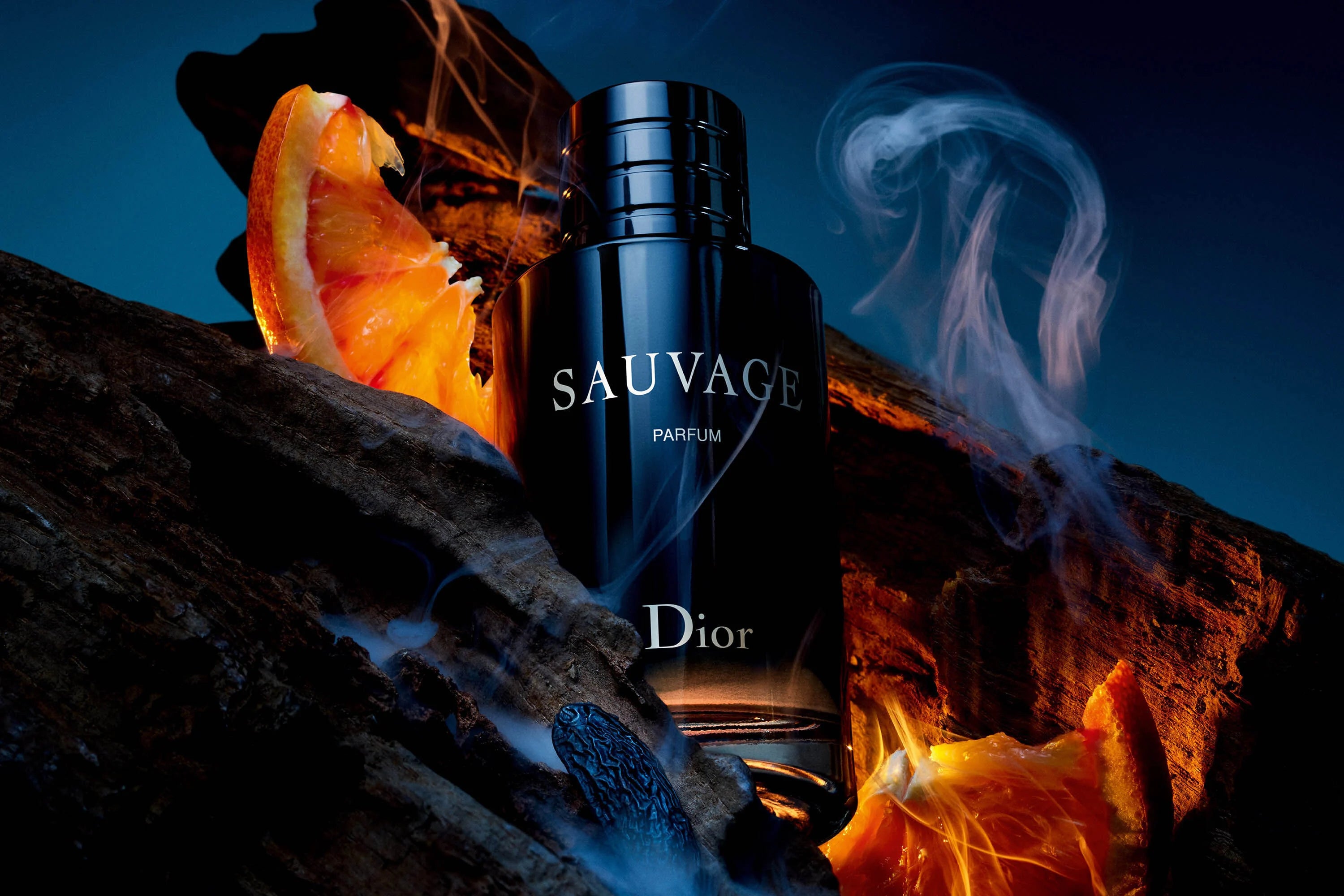 Dior Sauvage Perfume - 100ml Eau de Parfum surrounded by orange slices and smoky wood, illustrating its citrus and woody fragrance notes.