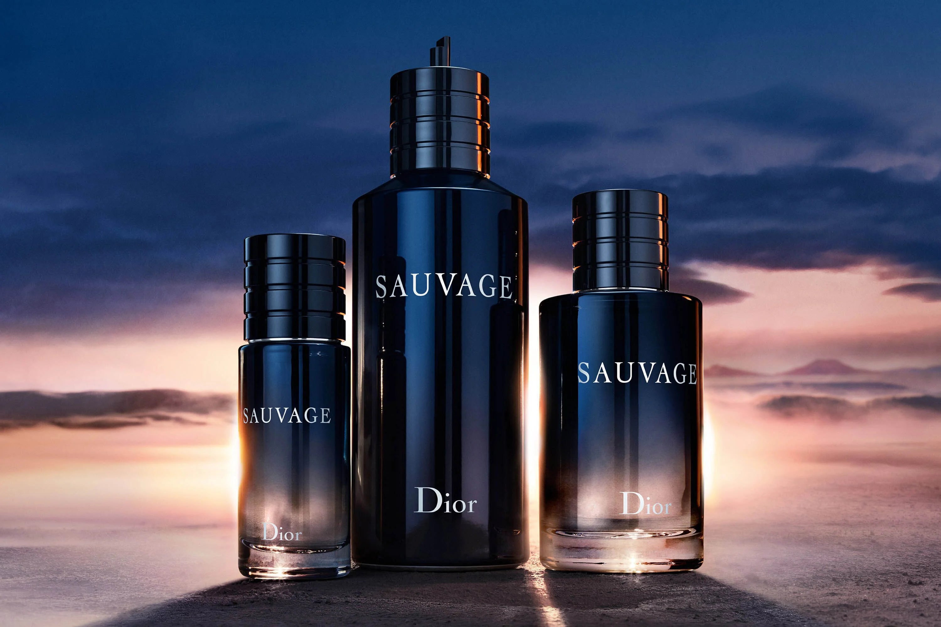 Three Dior Sauvage Perfume bottles in varying sizes set against a glowing horizon, representing the Eau de Parfum’s versatility and luxury.
