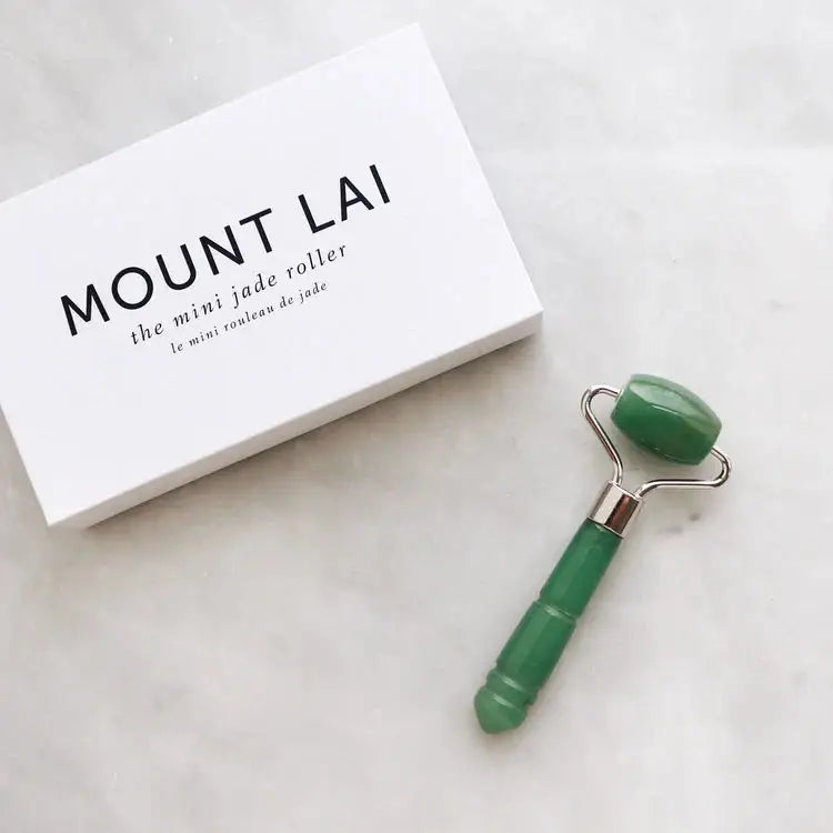 Mount Lai The De-Puffing Mini Jade Roller placed beside its branded packaging, showcasing its high-quality jade construction for soothing facial massage.