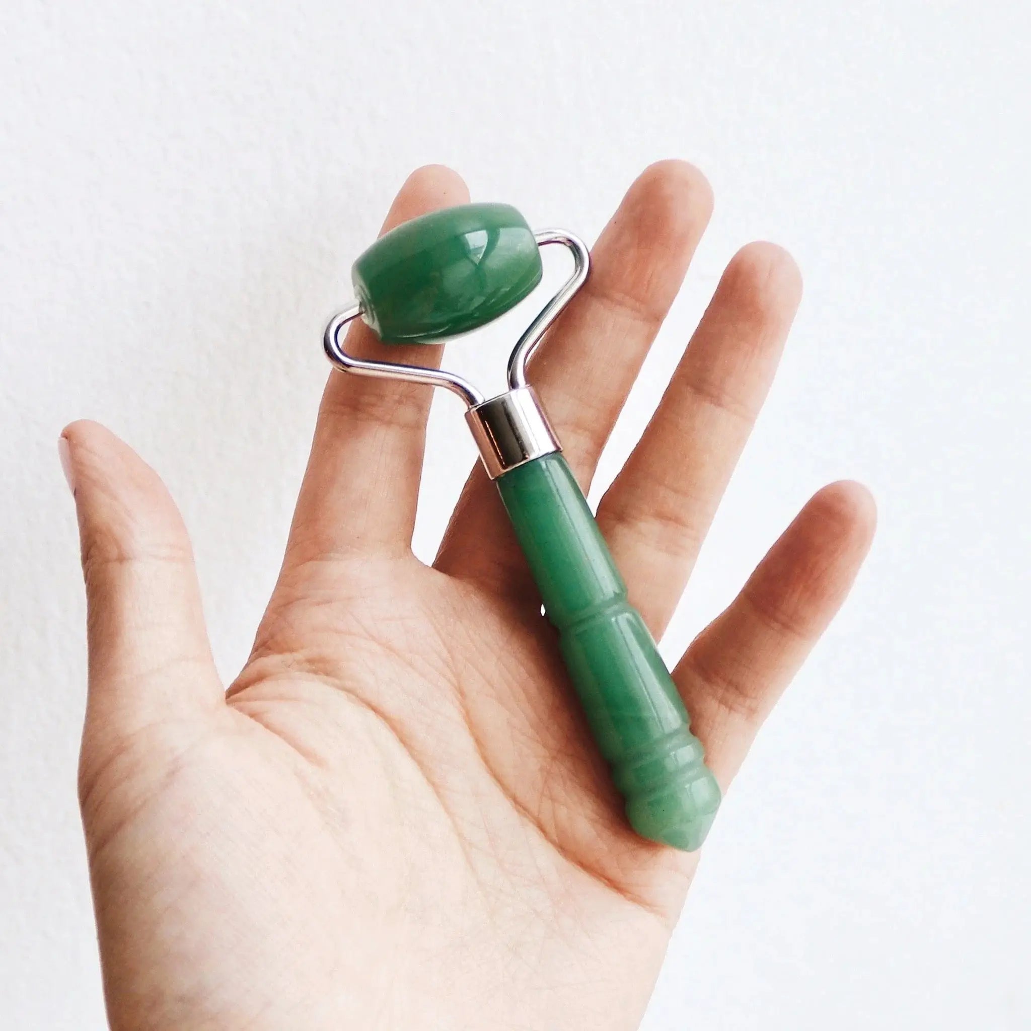 A hand holding the Mount Lai The De-Puffing Mini Jade Roller, demonstrating its compact size and ergonomic design for easy facial massage application.